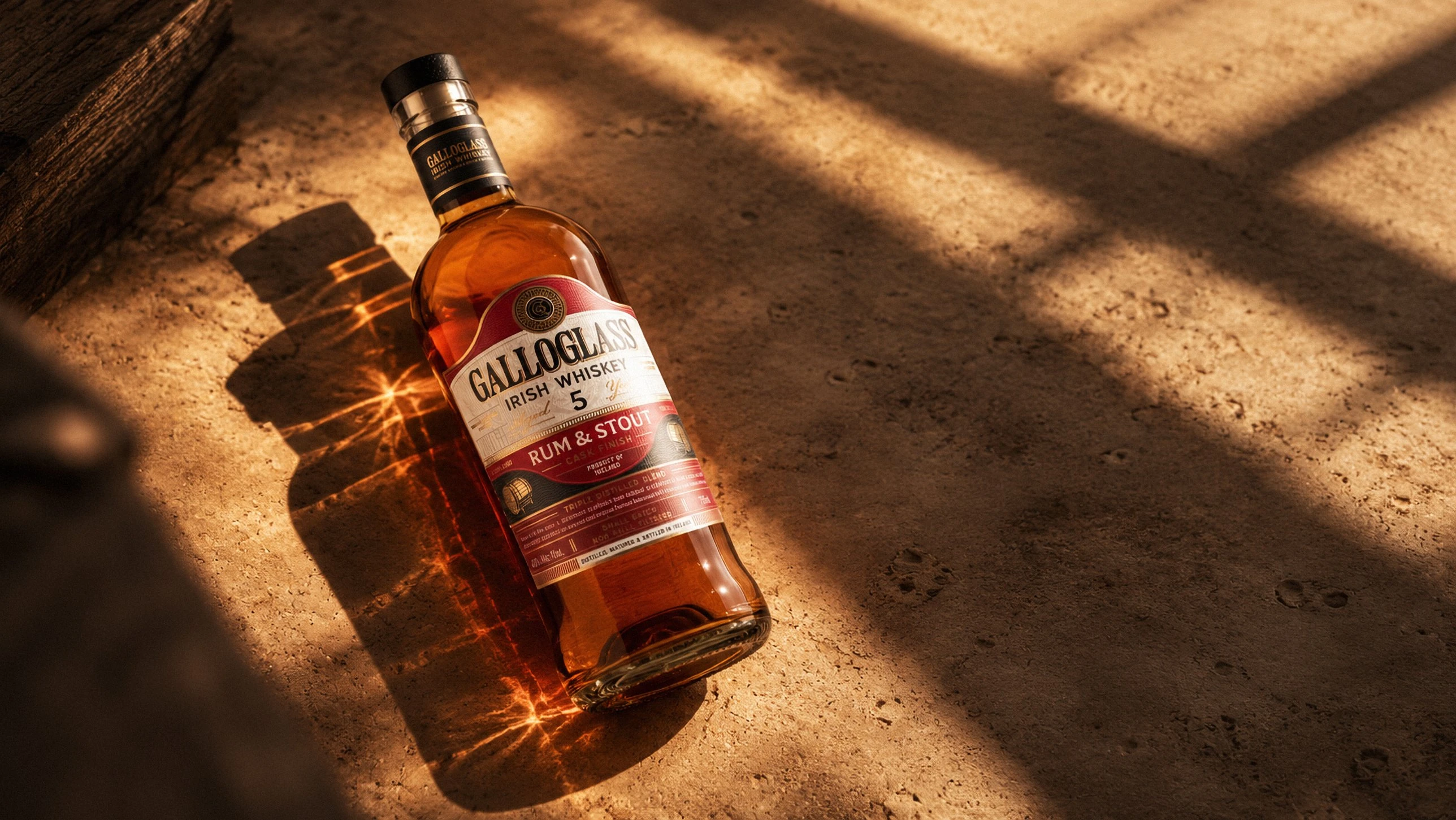 A bottle of Galloglass 5 Year Rum and Stout lying on a cork floor in warm window light